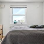 Bedroom with bed, window, and dresser. Two green bottles sit on the windowsill.