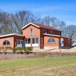 New brick building with large windows and garden. Construction site in background.