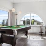 Pool table with green felt and balls. Large windows with view of the landscape.