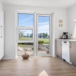 Kitchen with view of green field and water through large windows.