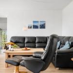 Living room with black leather sofa, wooden table, and chair. Wall has pictures and a wreath.