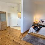 Schlafzimmer mit Bett, Nachttisch, Lampe und Kleiderschrank. Holzfußboden und Teppich.