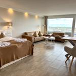 Schlafzimmer mit Bett, Sofa, Tisch und Blick auf Balkon.