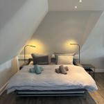 Schlafzimmer mit Doppelbett, zwei Stehlampen und Holzboden unter schrägen Wänden.