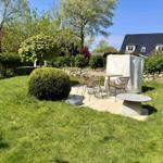 Garten mit Sitzbereich, Tisch, Stühlen und Beete. Hintergrund: Haus und Bäume.