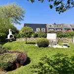 Garten mit Grill, Sitzgruppe und Blumenbeeten. Hintergrund: Wohnhäuser und Bäume.