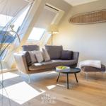 Wohnzimmer mit Sofa, Couchtisch und Fenster. Wanddekoration und Pflanze sichtbar.