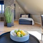 Schlafzimmer mit Dachschräge, Bett, Stehlampe und Pflanze. Tisch mit Früchten im Vordergrund.