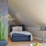 Schlafzimmer mit Dachschrägen, blauem Sofa, Holzboden und Pflanze.
