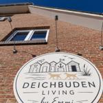 Schild an Backsteinmauer mit Strandhaus-Illustration und Text DEICHBU DEN LIVING