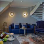 Ein Wohnzimmer mit blauem Sofa, Sessel und Treppe. Auf dem Tisch stehen Obst und Gläser.