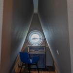 Ein kleiner Raum mit schrägen Wänden, einem runden Fenster und einem blauen Stuhl vor einem Schrank.