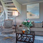 Wohnzimmer mit Sofa, Sessel, Tisch und Treppe. Wandbild zeigt Strand.