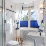 Badezimmer mit Dusche, Toilette, Waschbecken und Fenster mit blauen Jalousien.
