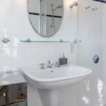 Badezimmer mit Waschbecken, Spiegel und Dusche. Weiße Fliesen und blaue Akzente.