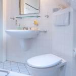 Badezimmer mit Waschbecken, Spiegel und Toilette. Weiße Fliesen und moderne Ausstattung.