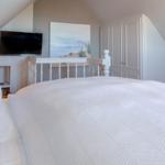 Schlafzimmer mit weißem Bett, Fernseher und Garderobe unter Dachschräge.