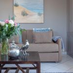 Ein Wohnzimmer mit Sofa, Couchtisch und Wandbild. Blumen und Dekorationen sind vorhanden.