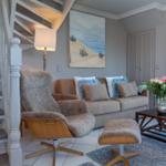 Wohnzimmer mit Sofa, Sessel und Tisch. Hintergrund: Wandgemälde und Treppe.