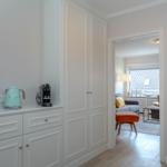 Küchenzeile mit Kaffeemaschine und Kessel. Durchgang in Wohnzimmer mit Sofa und Hocker.