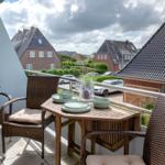 Balkon mit Tisch und zwei Stühlen, Blick auf Wohnhäuser und Straße.