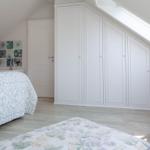 Schlafzimmer mit Dachschrägen, weißem Schrank und Bett mit Muster