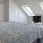 Schlafzimmer mit Dachschrägen, zwei Dachfenstern, Bett, Kleiderschrank und Fernseher.
