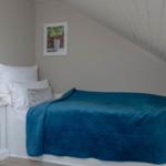 Ein Bett mit blauer Decke, Nachttisch und Wandbild unter schrägem Dach