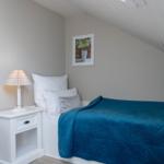 Schlafzimmer mit Dachschräge, blauer Bettdecke und Nachttisch mit Lampe.