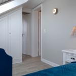 Schlafzimmer mit blauem Bett, weißem Schrank und Nachttisch mit Lampe.
