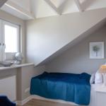Ein Schlafzimmer mit Dachschrägen, blauer Bettwäsche und Holzboden.