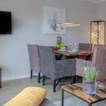 Esszimmer mit Holztisch, grauen Stühlen und Wandbild. Fernseher und Beistelltisch im Vordergrund.