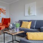 Ein Wohnzimmer mit grauem Sofa, orangefarbenem Sessel und modernen Kunstwerken an den Wänden.