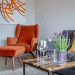 Ein Wohnzimmer mit orangefarbenem Sessel, grauem Sofa und Holztisch.