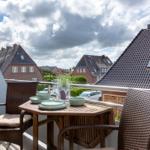 Terrasse mit Tisch und Stühlen, Blick auf Dächer und Himmel.