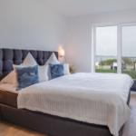 Schlafzimmer mit großem Bett, Fensterblick auf Wasser und Fernseher an der Wand.