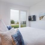 Schlafzimmer mit Bett, TV und Blick auf Grünfläche und Wasser.