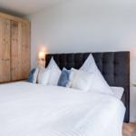 Schlafzimmer mit Bett, Holzschrank und Nachttisch mit Pflanze.