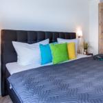 Schlafzimmer mit Bett, Kissen und Holzschrank. Beleuchtung und Blumen sind sichtbar.
