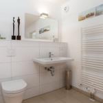Badezimmer mit Toilette, Waschbecken und Heizkörper. Wandbilder und Pflanze sichtbar.