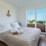 Bedroom with water view, bed with white pillows and wooden floor.