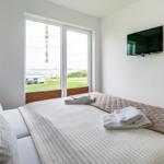 Bedroom with bed, TV, and view of green area and water.