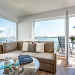 Living area with sofa, glass table, and view of water and terrace.