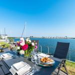 Table with flowers and food on terrace with view of water and sailboats.