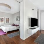 Schlafzimmer mit Bett, Wandbildern und Teppich. Wohnbereich mit Fernseher und Wandregal.