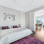 Schlafzimmer mit Bett, Wandbild und Blick in Wohnbereich mit Tisch und Sitzgelegenheiten.
