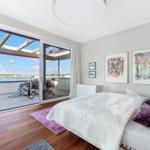 Schlafzimmer mit Balkon und Blick auf Wasser. Bett, Kunstwerke und Holzboden.