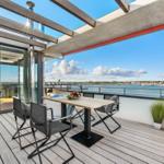 Terrasse mit Tisch, Stühlen und Meerblick. Holzdielen und Pflanzen.