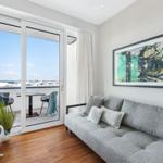 Ein Wohnzimmer mit grauem Sofa, Holzboden und Balkon mit Tisch und Stühlen.