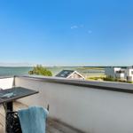 Terrasse mit Tisch und Stühlen, Blick auf Wasser und moderne Gebäude.